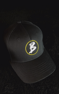 Schwarze Baseballkappe mit gelbem Kreis und weißem Schriftzug 'B' auf der Vorderseite.